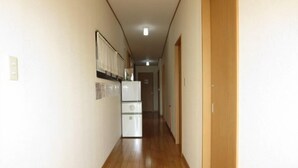 Un couloir étroit au plancher de bois, avec un réfrigérateur et une porte au fond.
