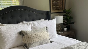 A neatly made bed with a patterned bedspread, a tufted headboard, and a bedside table with a lamp and a plant. - Charming 2-bedroom house, quiet neighborhood, in SoKno minutes from downtown (Knoxville)
