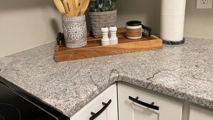 A kitchen counter with a wooden tray holding kitchen utensils, a decorative container, a salt and pepper set, a jar of citrus lavender, and a paper towel holder. - Charming 2-bedroom house, quiet neighborhood, in SoKno minutes from downtown (Knoxville)
