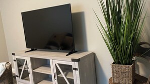 A wooden TV stand with a flat-screen TV, a potted plant, and a wall-mounted sign. - Charming 2-bedroom house, quiet neighborhood, in SoKno minutes from downtown (Knoxville)