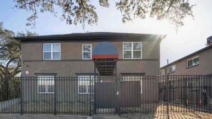 A two-story building with a basketball court in front, surrounded by a metal fence. - 1BR The Raven Flats! A Hermann Park! Med Center! (Houston)