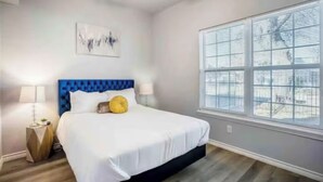 A bedroom with a bed, a window with blinds, a ceiling fan, and a wall-mounted artwork. - 1BR The Raven Flats! A Hermann Park! Med Center! (Houston)