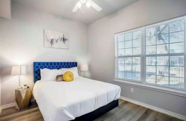 Un dormitorio con cama, ventana con persianas, ventilador de techo y una obra de arte en la pared.