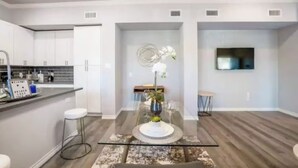 A modern kitchen with white cabinets, a bar area, and a dining space with a glass table and chairs. - 1BR The Raven Flats! A Hermann Park! Med Center! (Houston)