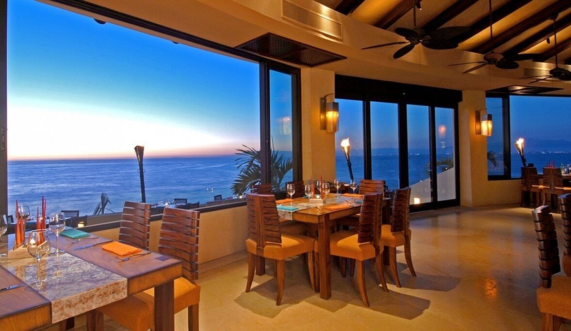 A dining area with a view of the ocean, large windows, and ceiling fans.