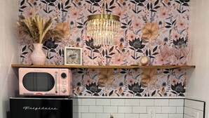 Una cocina con un refrigerador negro, gabinetes blancos, una encimera blanca, un salpicadero con motivos florales y una lámpara colgante.