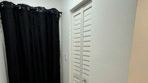 Un pasillo con cortina de ducha negra, puertas de armario blancas y suelo de madera.