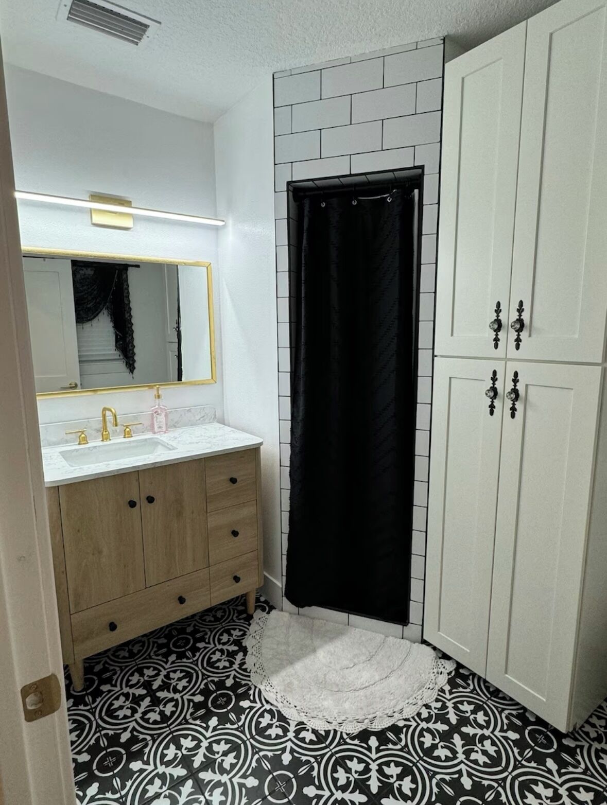 A bathroom with a white sink, wooden vanity, black and white patterned floor, and a white door with black handles.