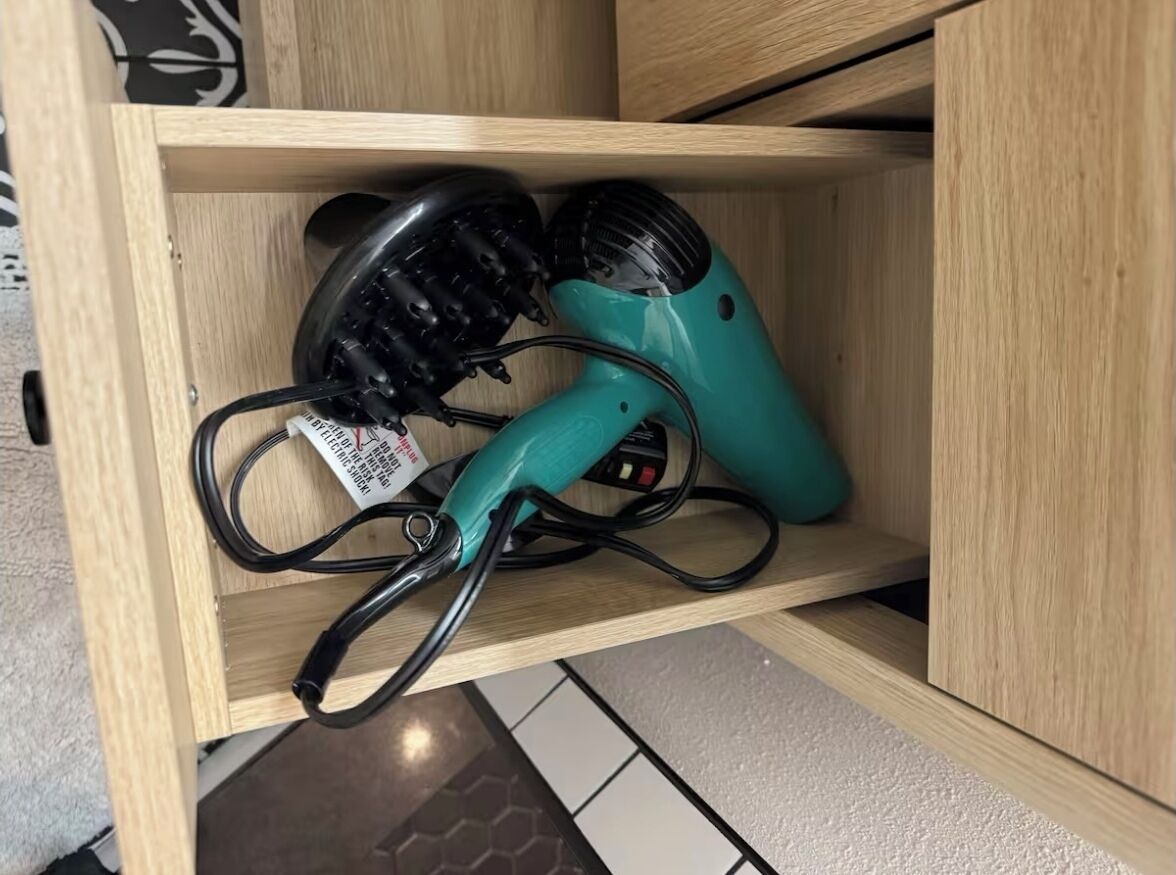A wooden cabinet with two hair dryers, one black and one teal, placed inside.