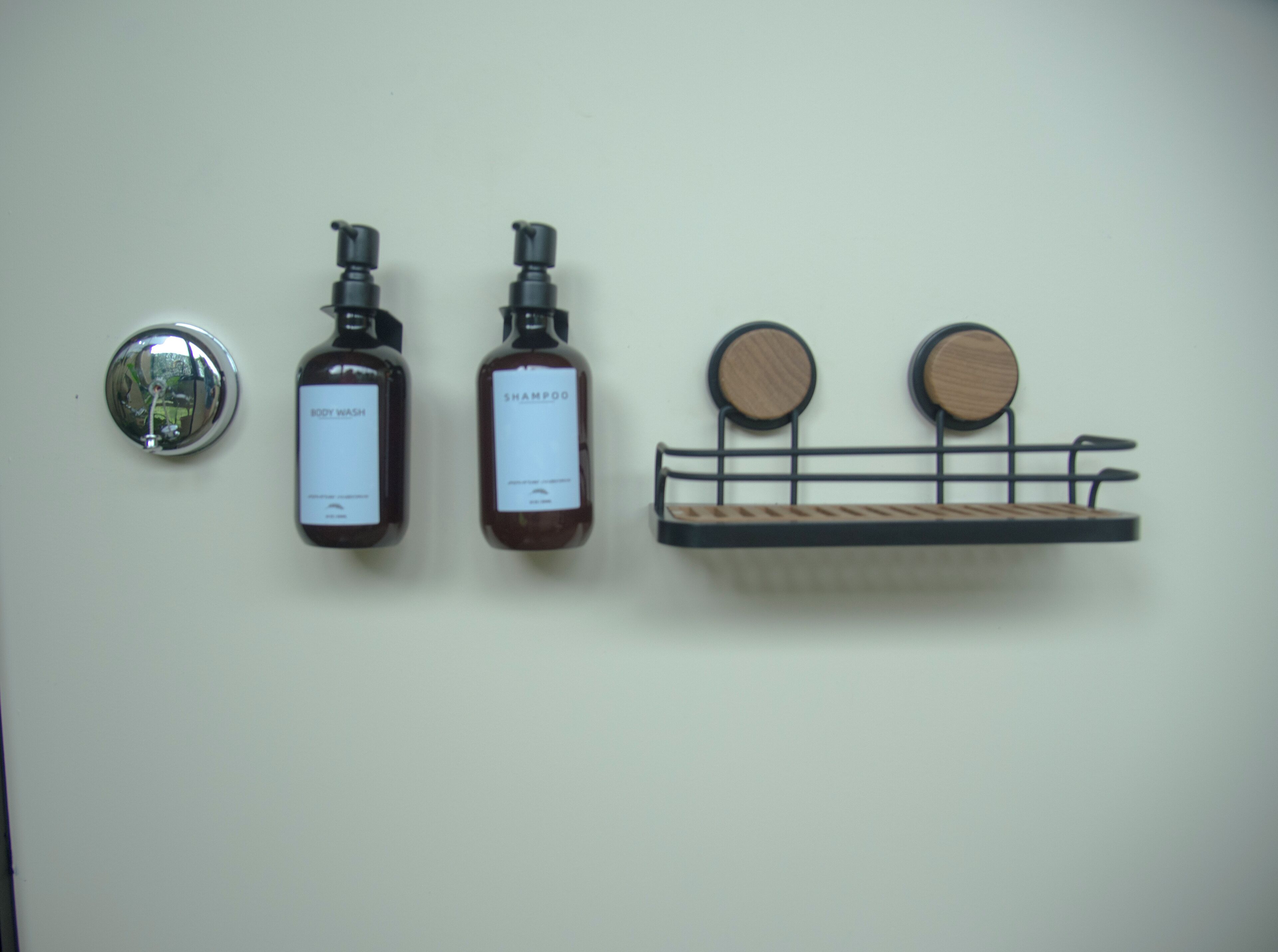 Twee flessen douche- en shampoosamenstelling op een muur, met een spiegel en een houten plank.