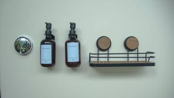 Twee flessen douche- en shampoosamenstelling op een muur, met een spiegel en een houten plank.