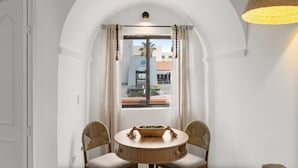 Una habitación con una mesa redonda y dos sillas, una ventana con cortinas y vistas a edificios.