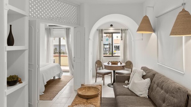 Una habitación moderna, con decoración blanca, un rincón de descanso acogedor, una mesa de comedor y vistas a través de un ventanal arqueado.