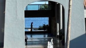 Un edificio moderno con una amplia entrada en arco, una fuente y vista al mar.