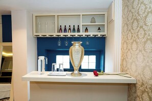 A bar area with a white countertop, a decorative vase, and a selection of bottles on shelves. - Hotel Santosi (San Luis Potosí)