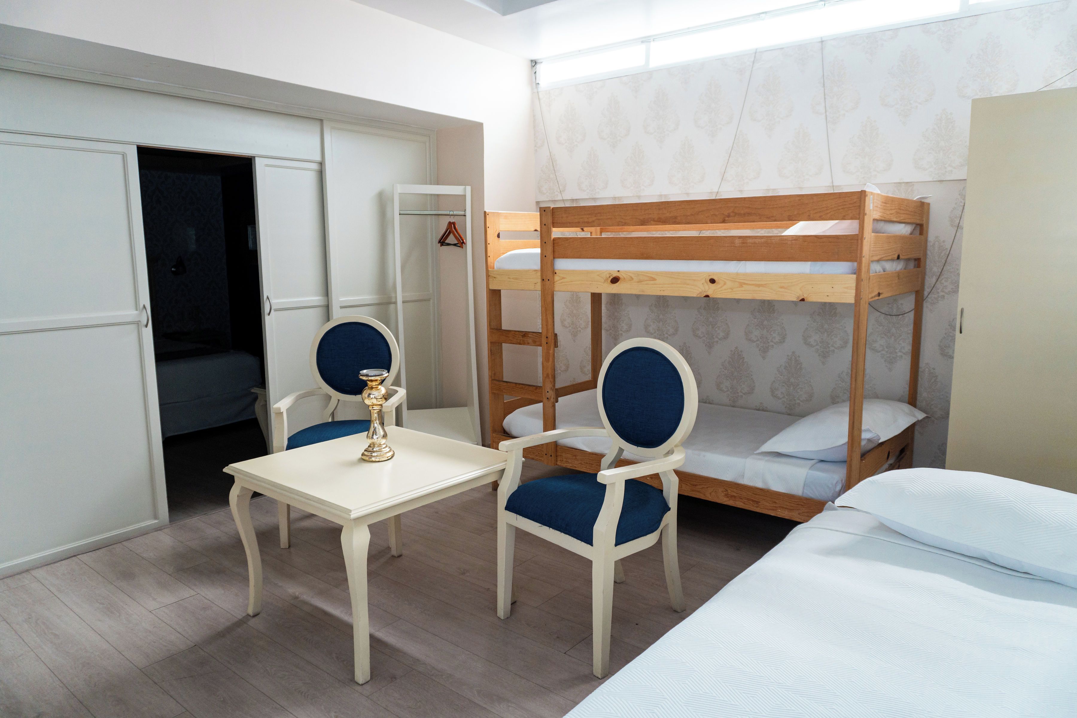 A room with bunk beds, a table, two chairs, and a hanging coat rack.