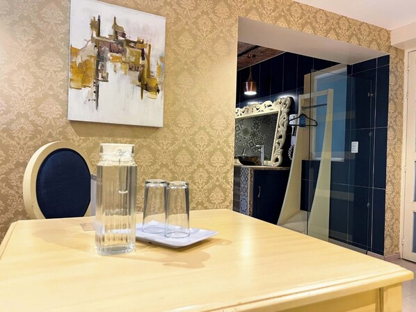 A hotel room with a dining table, a painting on the wall, and a bathroom visible through a glass door. - Hotel Santosi (San Luis Potosí)