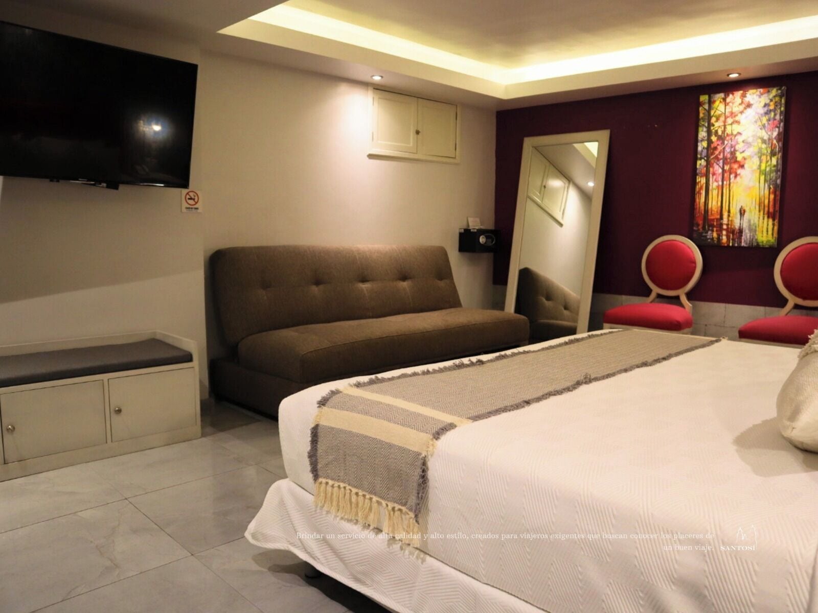 Een moderne hotelkamer met een groot bed, een bank, een flatscreen televisie, een spiegel en een rode stoel.