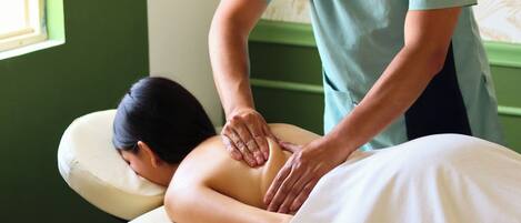 Une séance de massage dans une pièce dont un mur est peint en vert et qui possède une fenêtre.