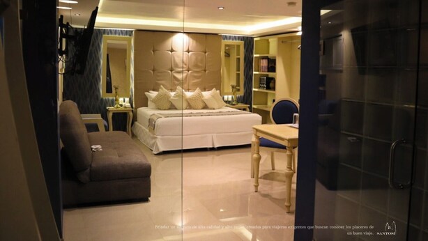 A modern hotel room with a large bed, a sofa, a desk, and a mirror. - Hotel Santosi (San Luis Potosí)