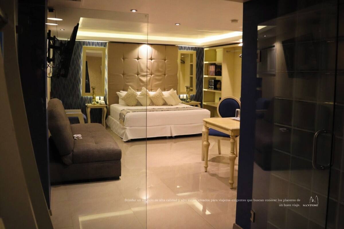 A modern hotel room with a large bed, a sofa, a desk, and a mirror.