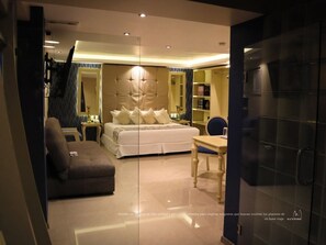 A modern hotel room with a large bed, a sofa, a desk, and a mirror. - Hotel Santosi (San Luis Potosí)
