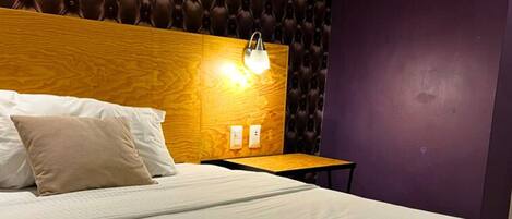 A hotel room with a wooden headboard, a bedside table, and a nightstand.