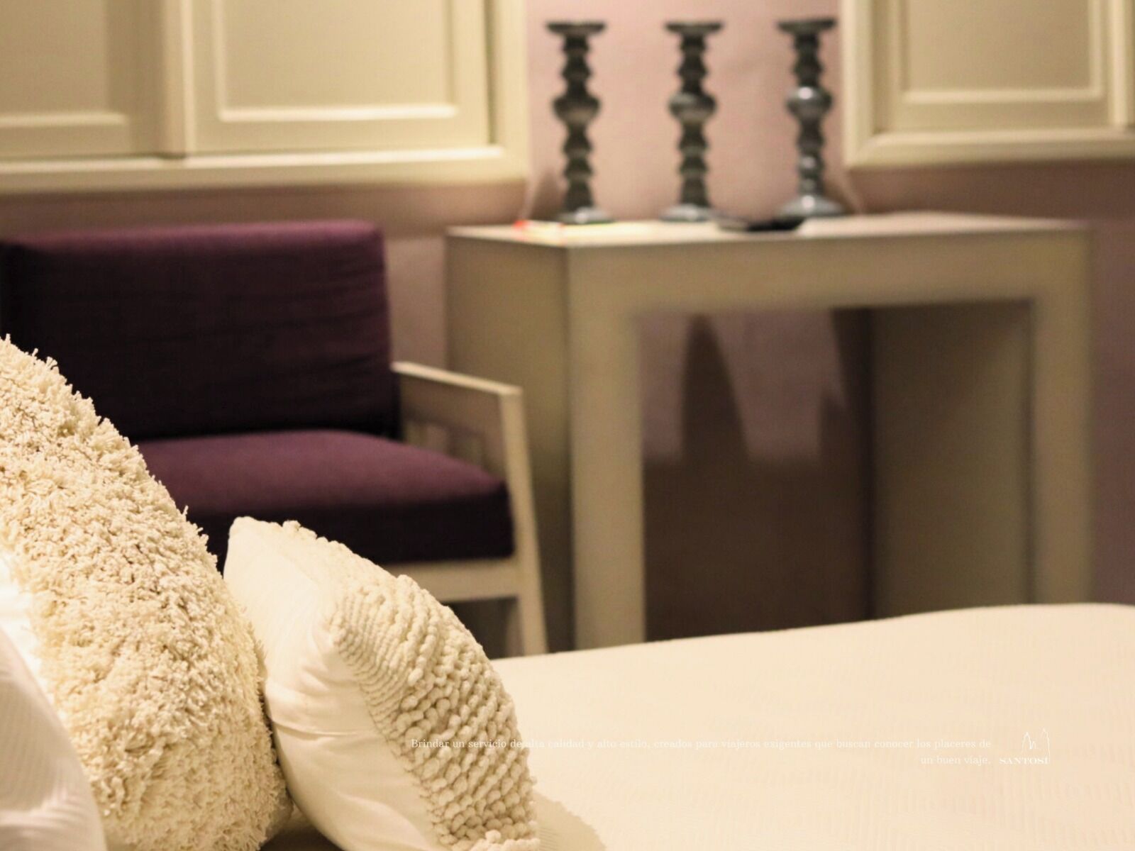 A hotel room with a bed, a chair, and a small table with a candle.