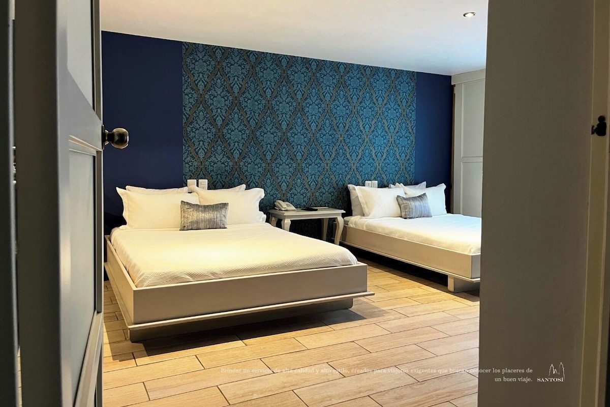 A hotel room with two beds, a patterned wall, and a wooden floor.