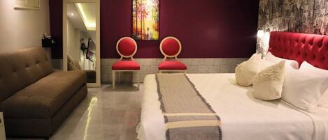 A modern bedroom with a large bed, two red chairs, a sofa, and a decorative wall piece.