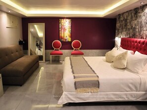 A modern bedroom with a large bed, two red chairs, a sofa, and a decorative wall piece. - Hotel Santosi (San Luis Potosí)