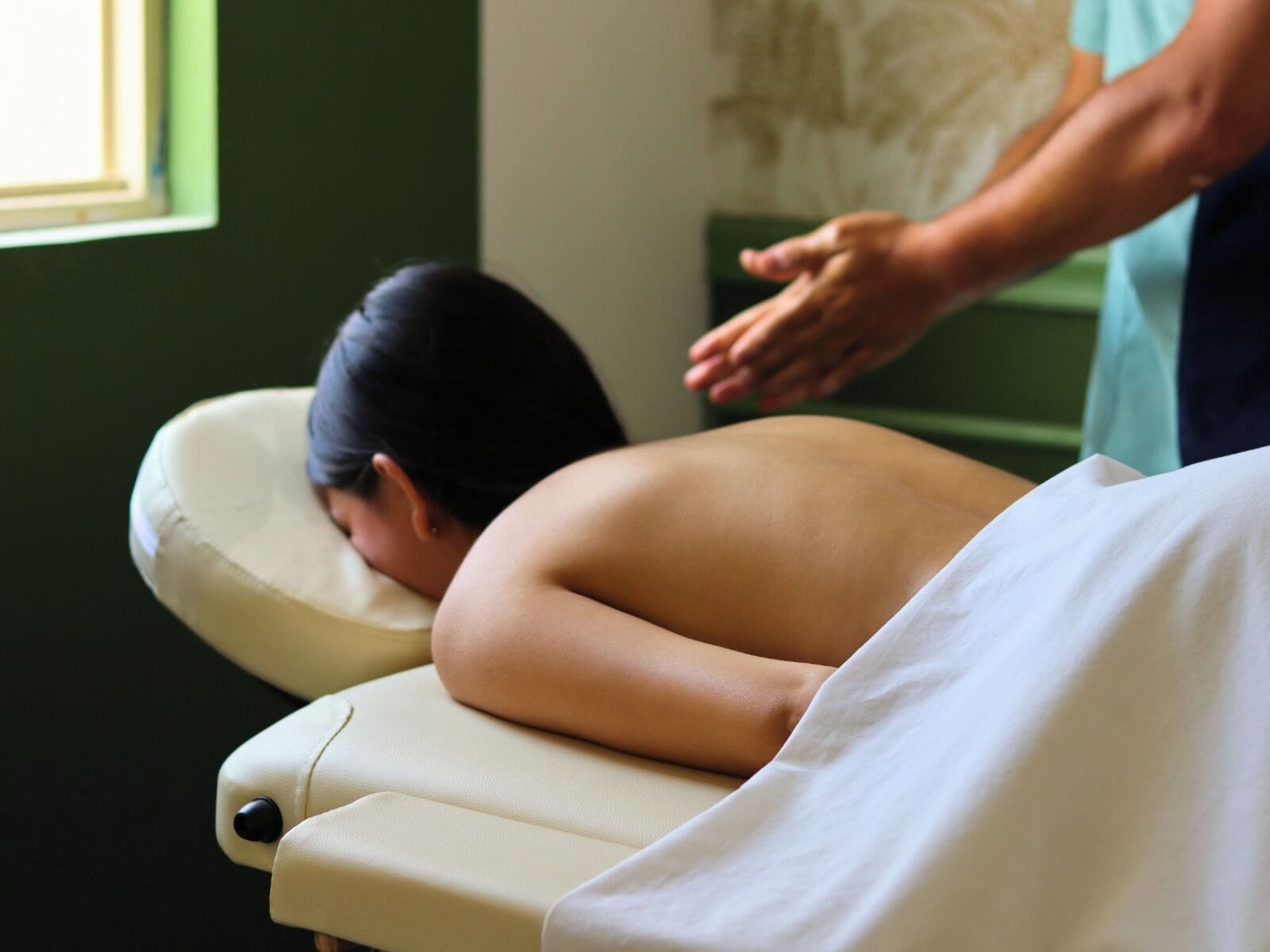 A massage therapy session in progress with a client lying face down on a treatment table.