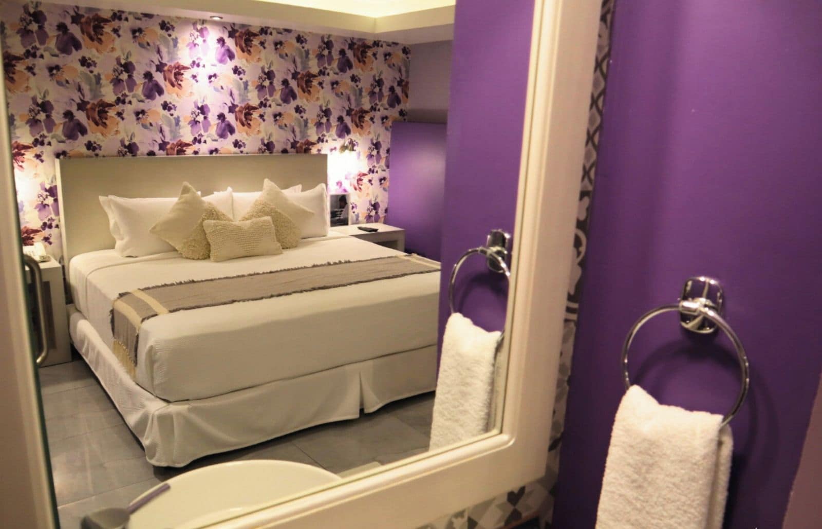 A hotel room with a large bed, a bathroom with a mirror, and purple walls.