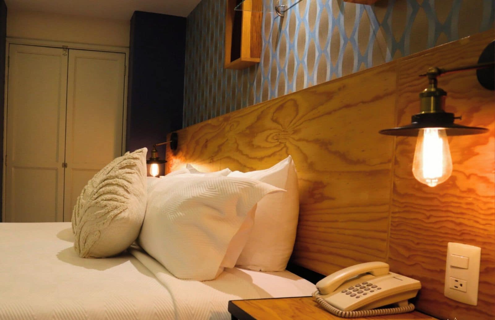 A hotel room with a bed, a bedside telephone, and a wall-mounted light fixture.