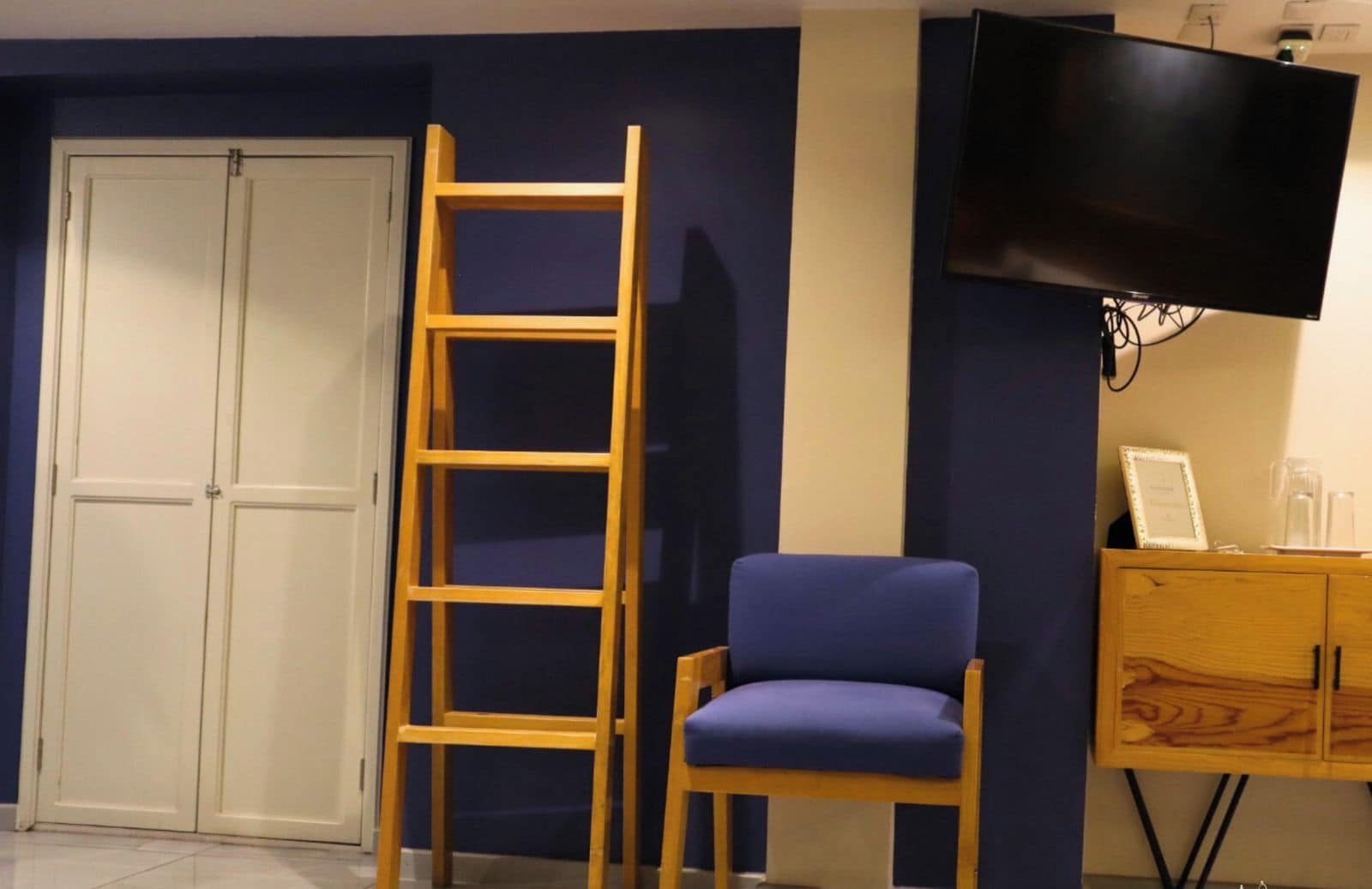 A room with a wooden ladder, a blue chair, a television, and a wooden cabinet.