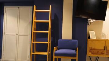 A room with a wooden ladder, a blue chair, a television, and a wooden cabinet.