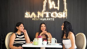 Tres mujeres sentadas en una mesa, con un letrero de paisaje urbano que indica que se trata de un restaurante.