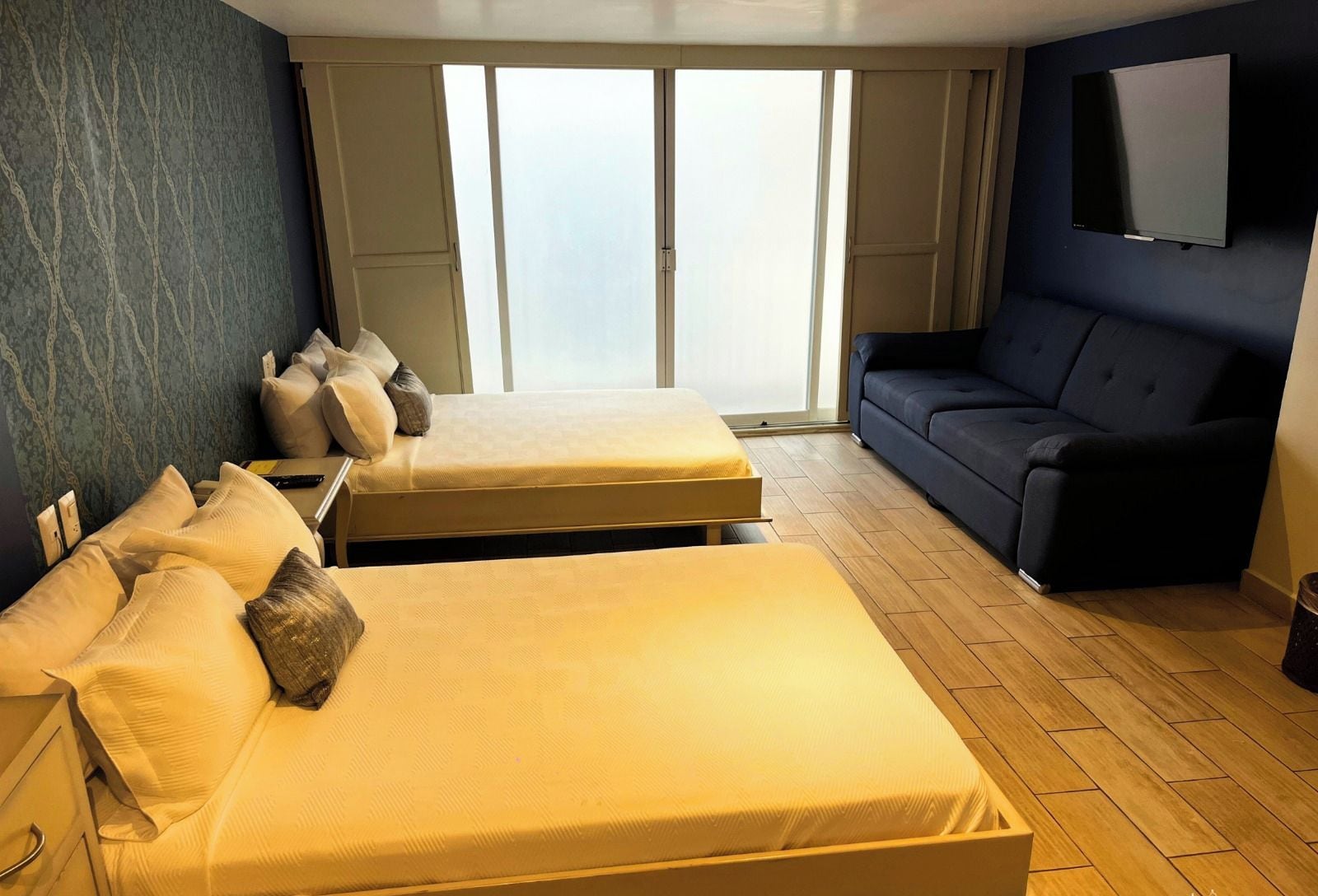 Ein Hotelzimmer mit zwei Betten, einem Sofa, einem Fernseher und einem großen Fenster.