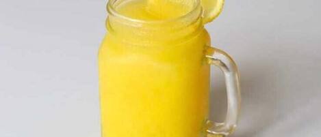 A clear glass pitcher with a handle, containing a yellow liquid, possibly a beverage, with a slice of lemon on the rim.