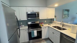 Una cocina moderna con gabinetes blancos, electrodomésticos de acero inoxidable, microondas, horno y lavavajillas.