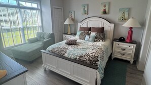 Un dormitorio con cama, ventilador de techo, ventana con persianas y una obra de arte en la pared.