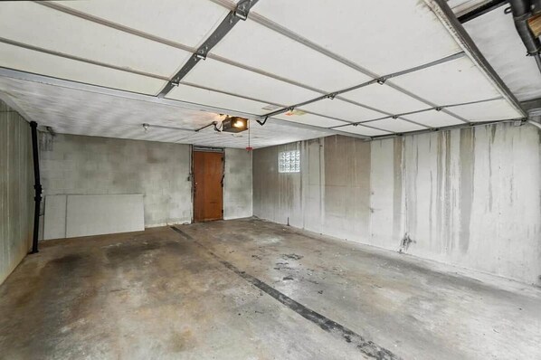 A large, empty room with concrete walls and a sloped ceiling, featuring a single door and a small window.