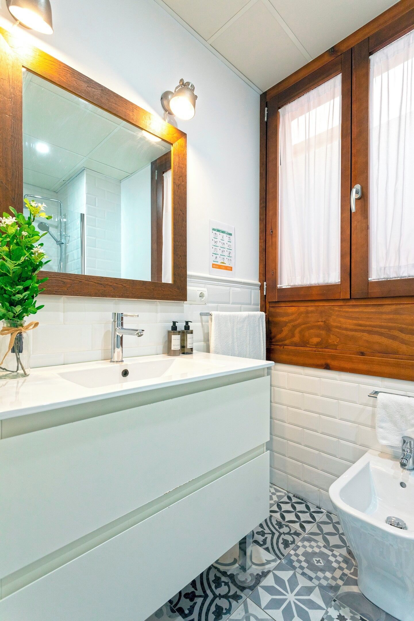 A bathroom with two sinks, a mirror, a window with curtains, and a patterned floor.