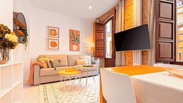 Un salon moderne avec un canapé, une table basse et un téléviseur. Des tableaux encadrés ornent le mur, et un mur de briques se trouve à l’arrière-plan.