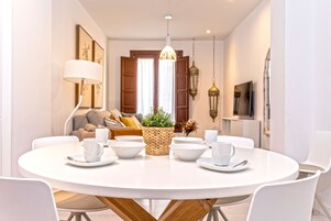 A dining area with a round table, white chairs, and a central woven basket with a plant.