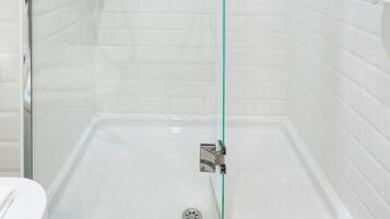 Cabina de ducha con paredes de vidrio, cabezal de ducha manual y grifo en la pared.