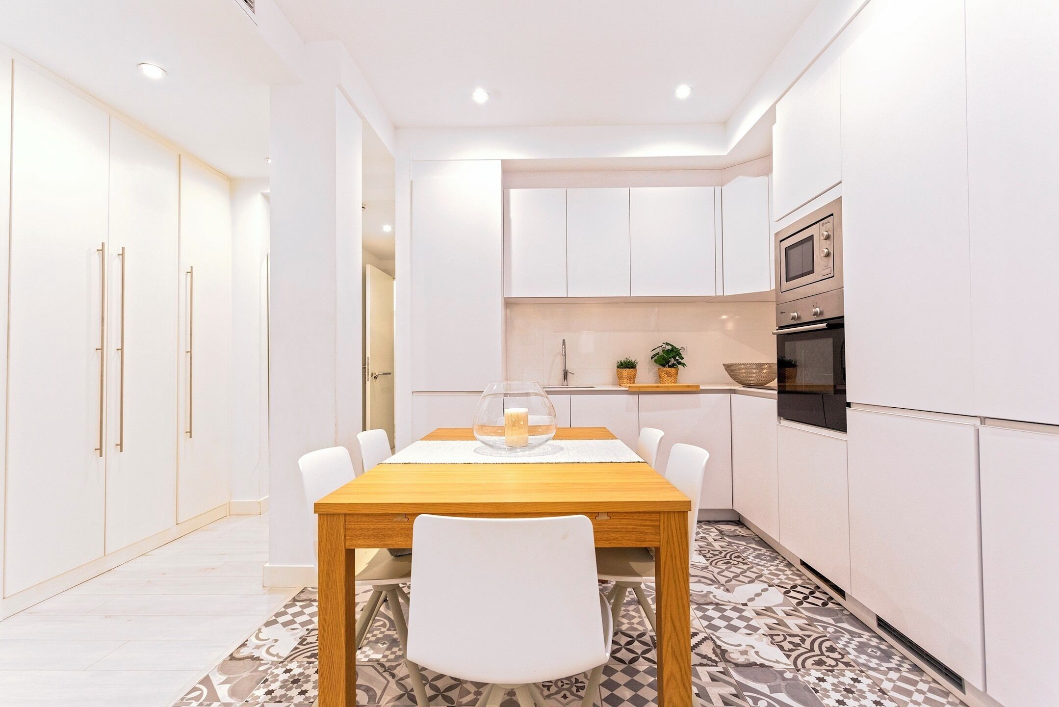 A modern kitchen with white cabinets, a wooden dining table, and a patterned floor.