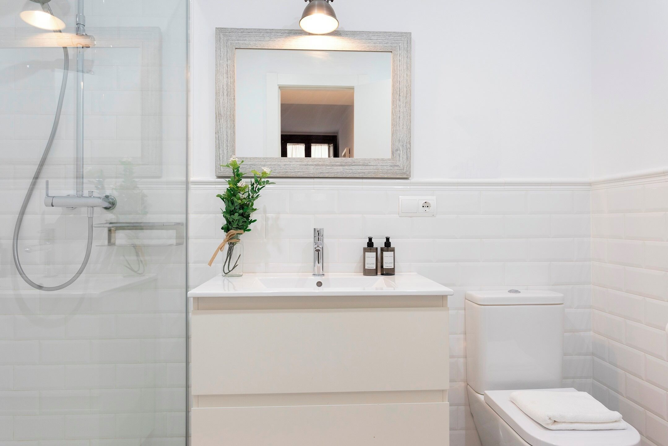 A modern bathroom with a glass shower enclosure, a white vanity with a mirror, and a toilet.