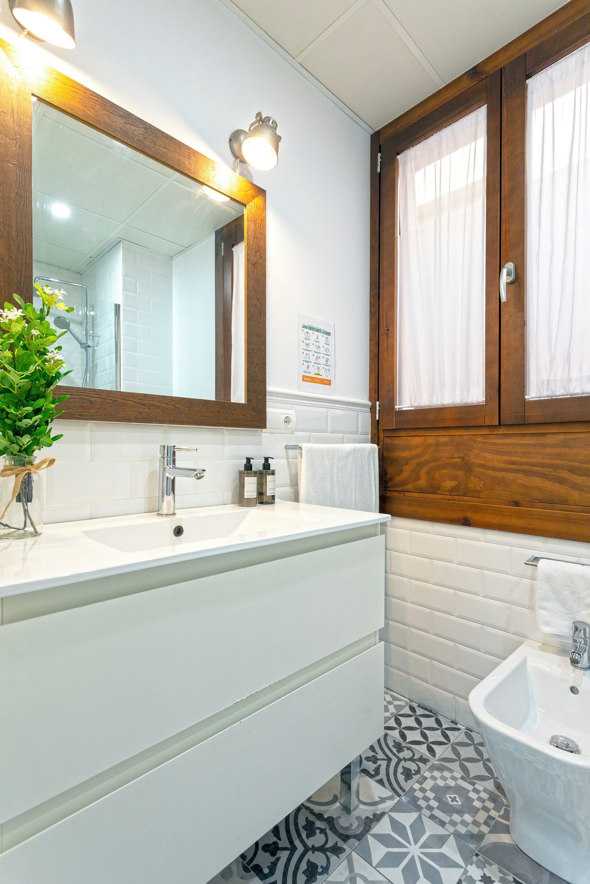 A bathroom with a double sink, a mirror, a wooden cabinet, and a small bathtub.