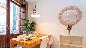 A dining area with a wooden table, white chairs, a hanging light fixture, a round mirror, and a white shelving unit. - Genteel Home Zacatín Granada (Granada)